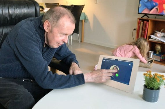 Mogens trykker på sin b-near® skærm, en brugervenlig telefon til ældre med Parkinson-demens
