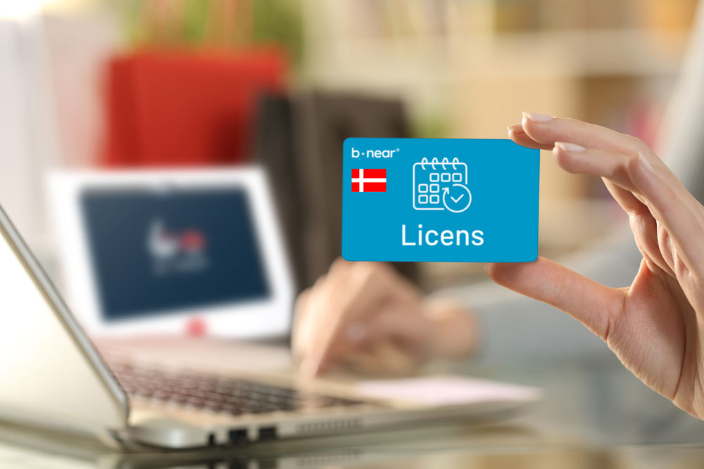 Hånd holder et b-near® licenskort foran computer og b-near® skærm som illustration af licensløsning